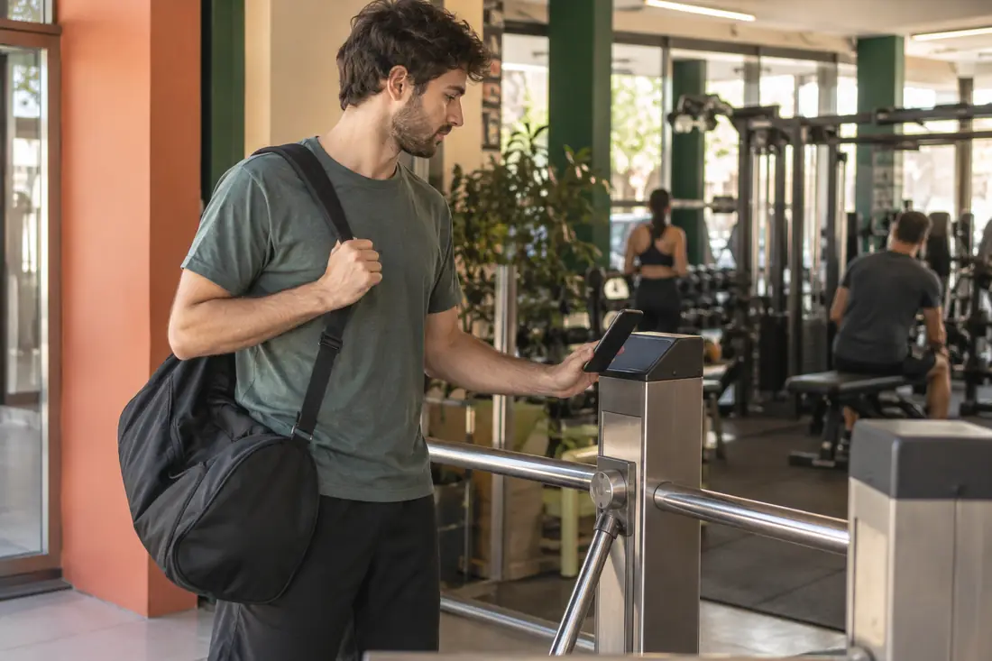 La entrada de un gimnasio: un alumno acerca el celular al lector del molinete para pasar.