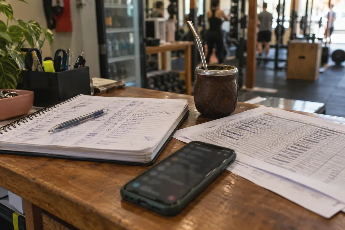 El mostrador de un gimnasio a fin de mes: un cuaderno de cuotas, una planilla impresa llena de tachones y el celular lleno de mensajes.